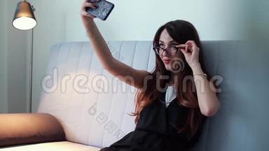 戴眼镜的年轻女孩在家里用智能手机自拍